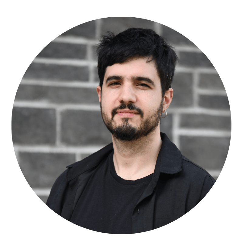 federico-ferreira-2026 A person with short black hair, a beard, and an earring stands in front of a gray brick wall, wearing a black shirt and jacket.