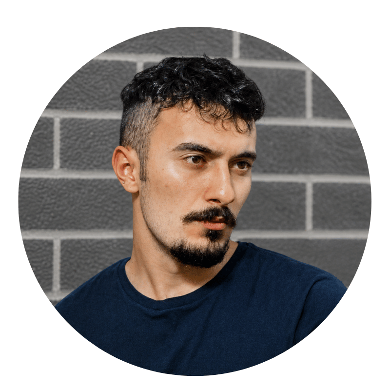 ramon-berrio-2026 A man with short, dark curly hair and facial hair wears a navy shirt and stands in front of a gray brick wall, looking slightly to the side.